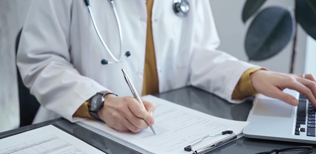 Doctor woman is working on laptop with medical reports. Healthcare professional reviews patient files and inputs data in a clinic setting. Medicine.